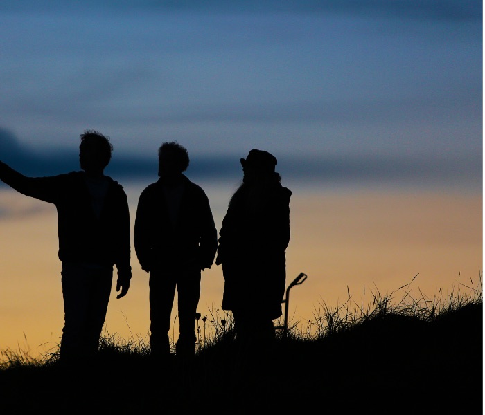 three people silhoetted at twilight against an orange and blue sky
