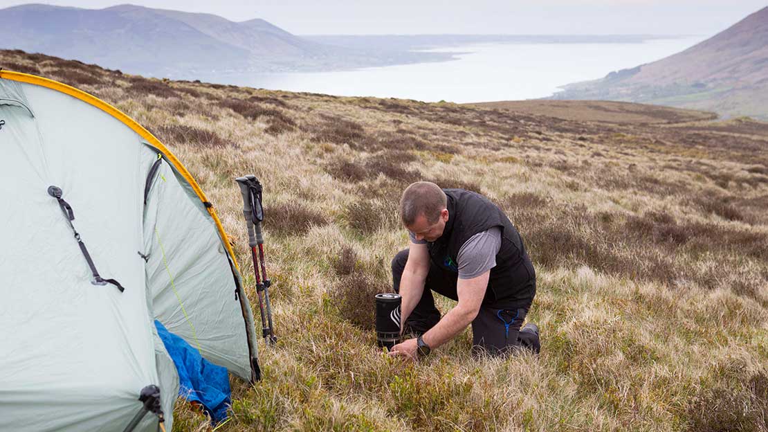 Mountain Ways Ireland guide lighting a jetboil on mountainside alongside tent 